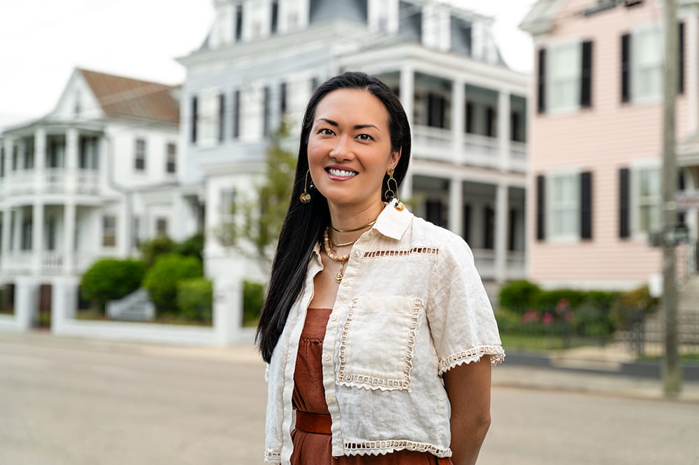 a stylish young woman poses in front of grand old homes of Charleston SC